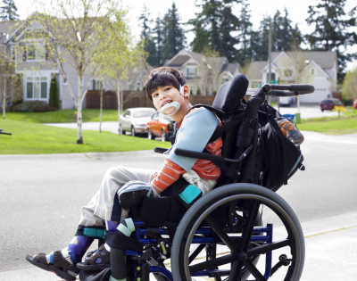happy boy waiting on sidewalk in wheelchair
